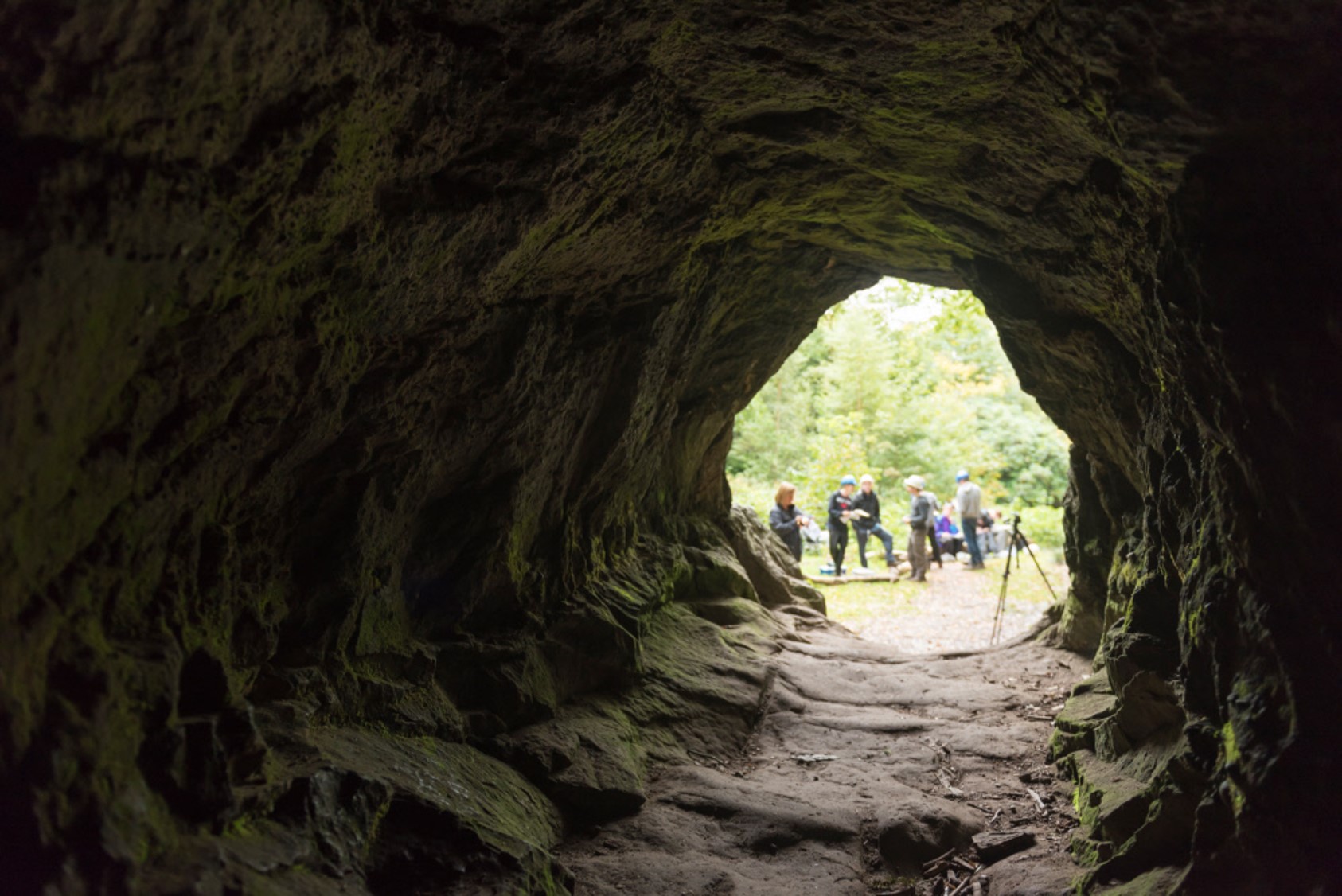 View of researchers talking outside the mouth of cave - by Paul Harris